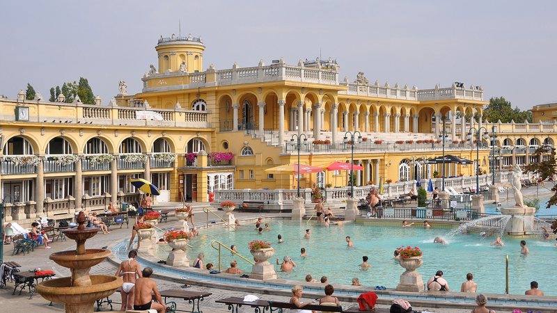 Het gele badgebouw en het buitenbad van het Széchenyi-bad